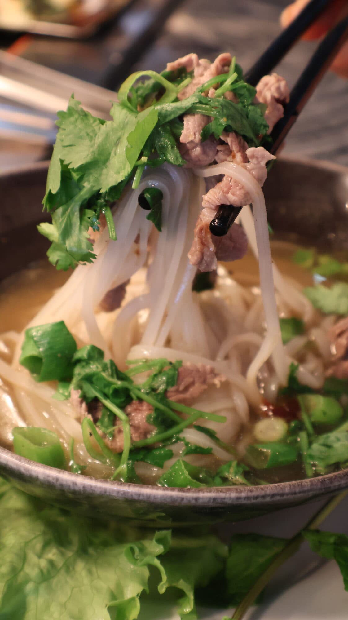 Bol de phở garni d'herbes fraîches et de baguettes, vapeur montante