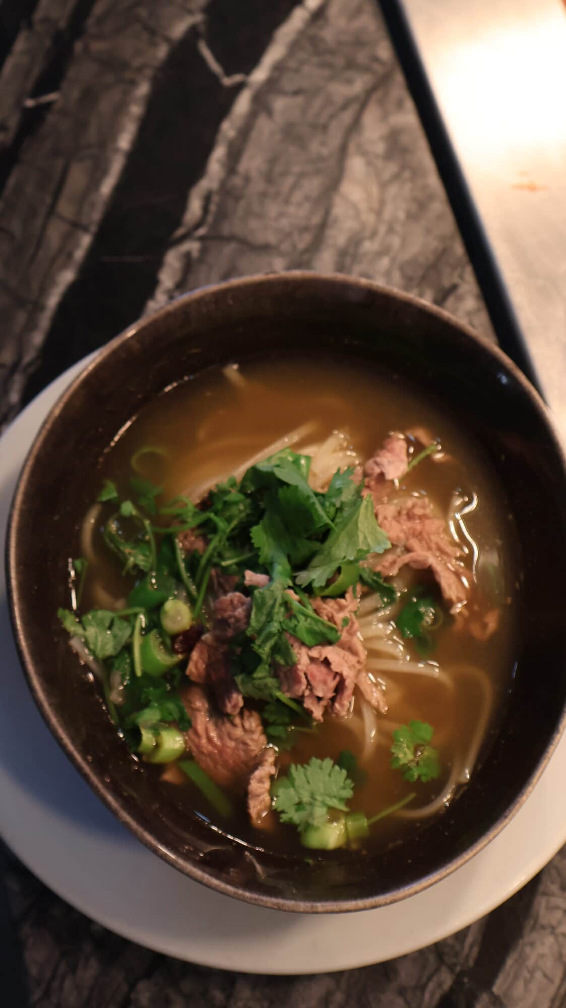 Bol de phở au bœuf fumant, bouillon ambré, coriandre et oignons nouveaux